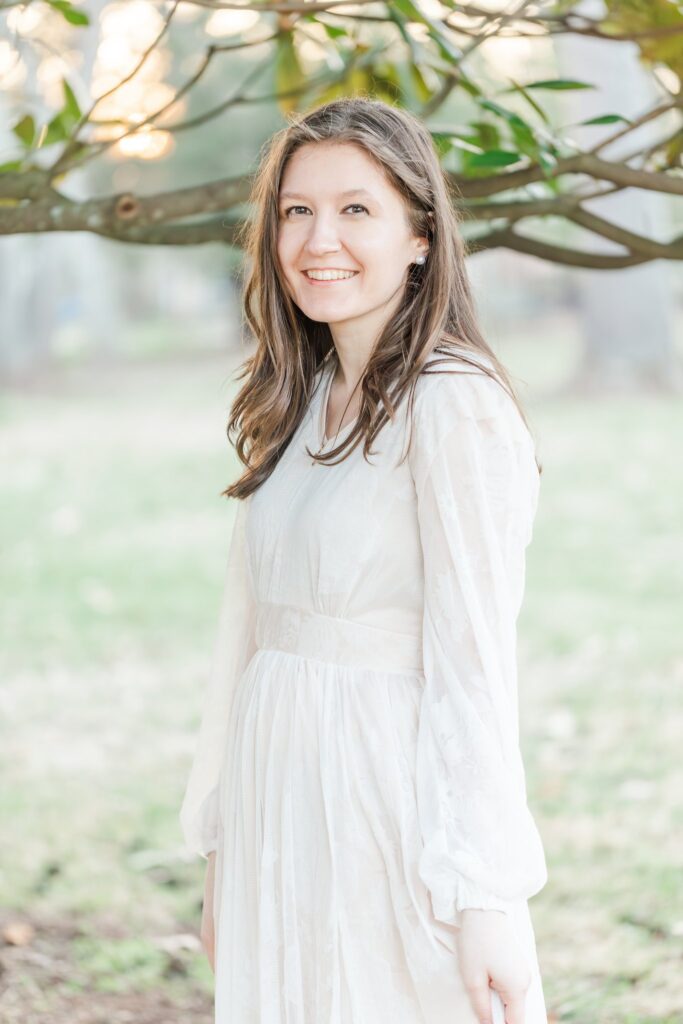 lady in white dress smiling with a green tree in the background