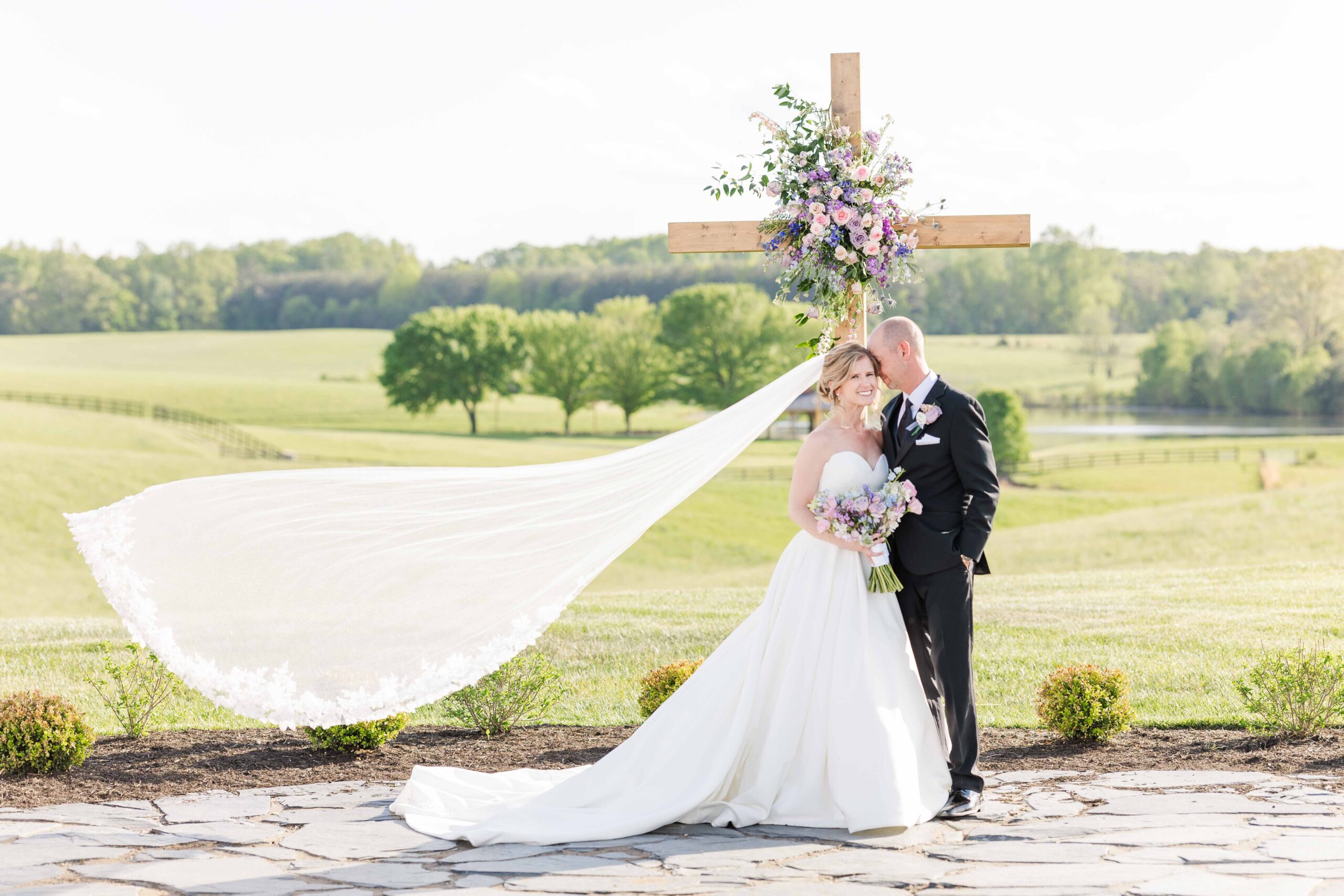 Epic, Cathedral Length veil flowing in the wind in front of a cross covered with lavender, lilac, and blush flowers!