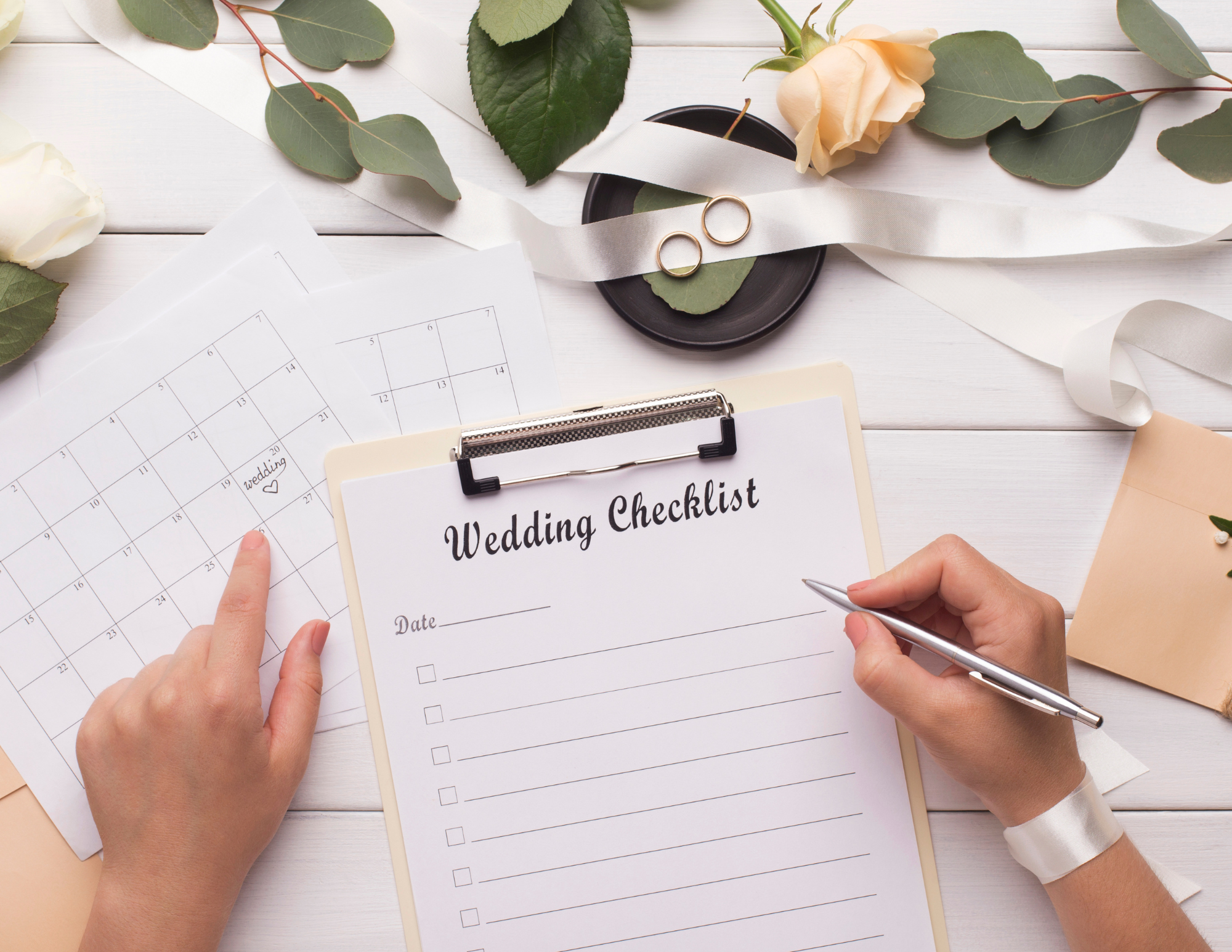 Wedding planning checklist with real florals in the background and wedding rings in a dish