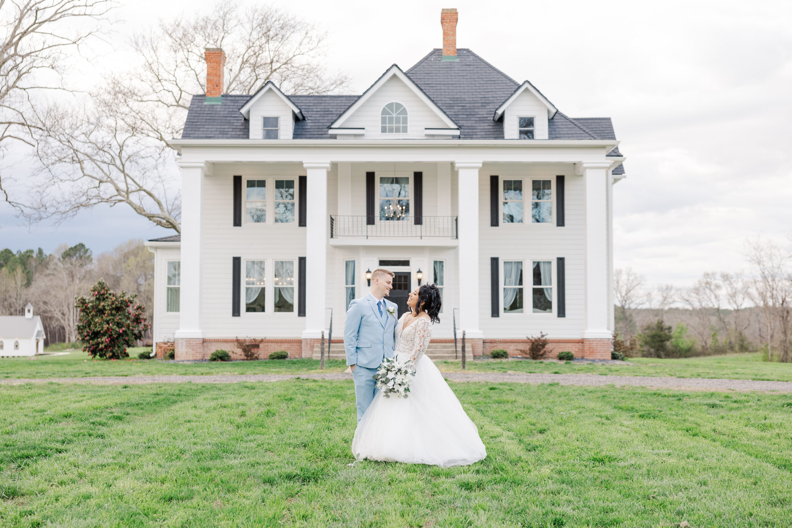 Bride and groom smiling at each other and standing in front of White Oak Manor in Dinwiddie, VA on their wedding day