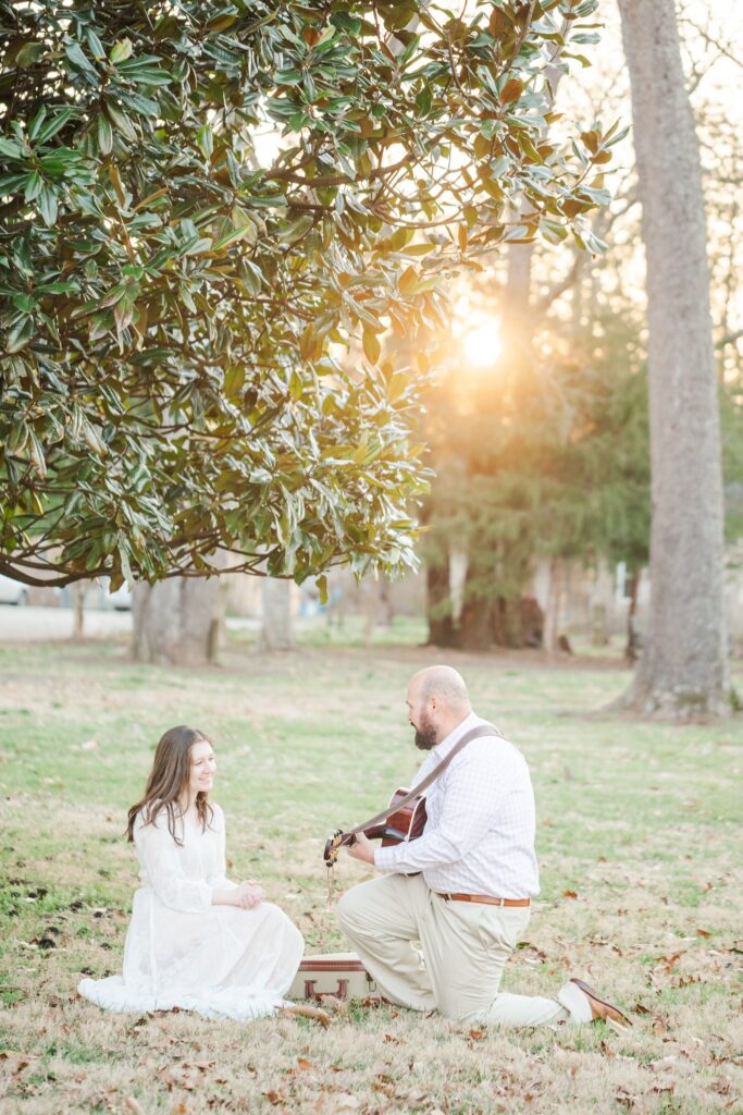 man playing guitar under magnolia tree with a lady in a white dress watching him
