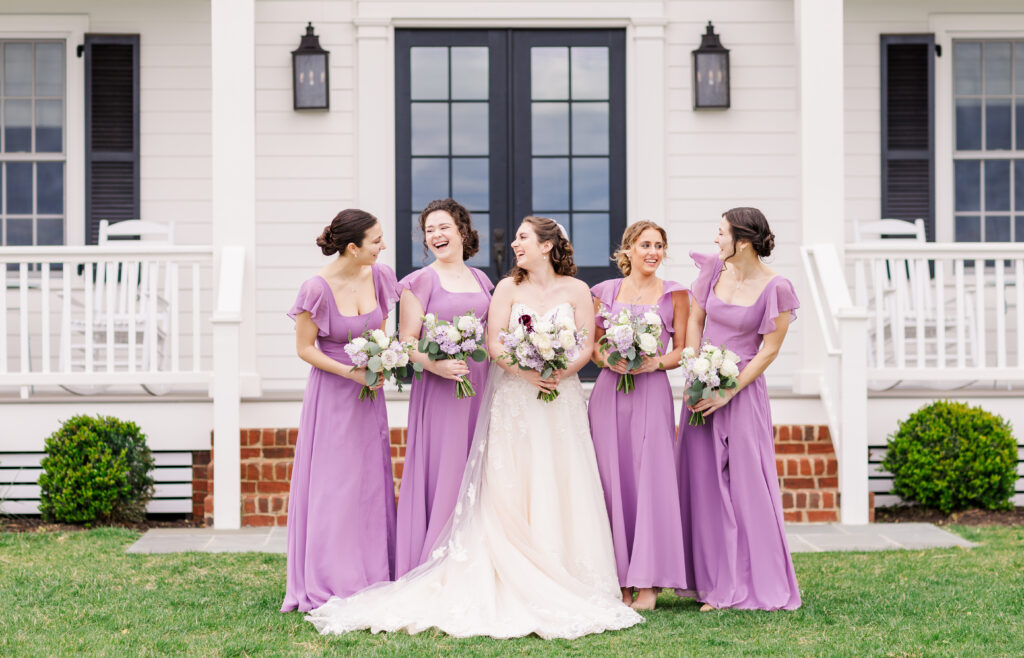 bride laughing with her bridesmaids on her wedding day with a manor house in the background