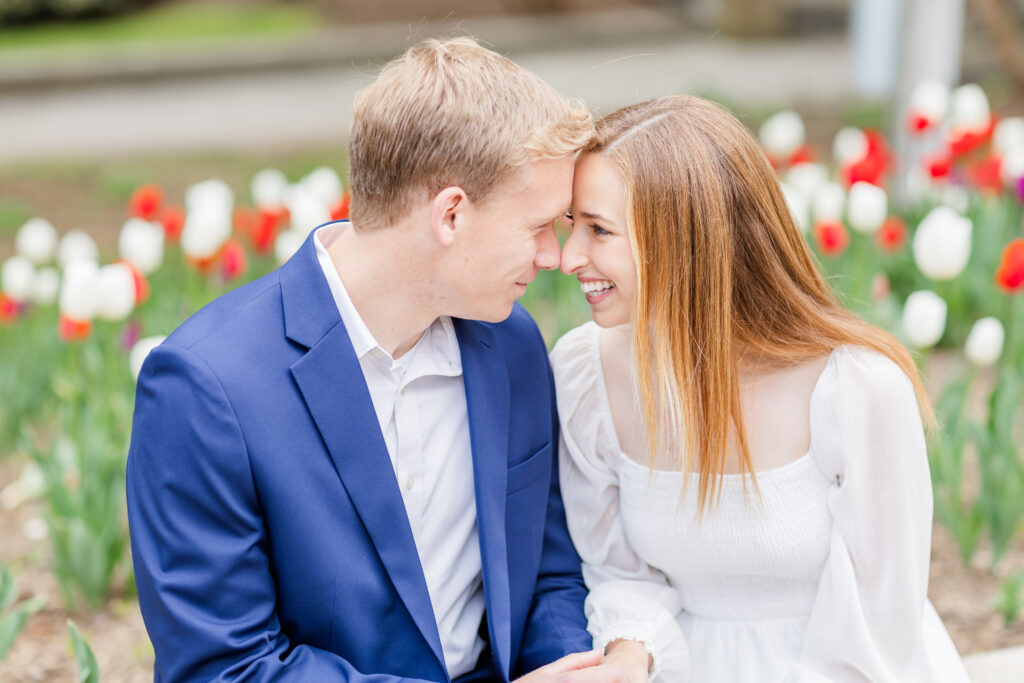 engaged couple smiling at each other with gorgeous red, white, and purple tulips in the background