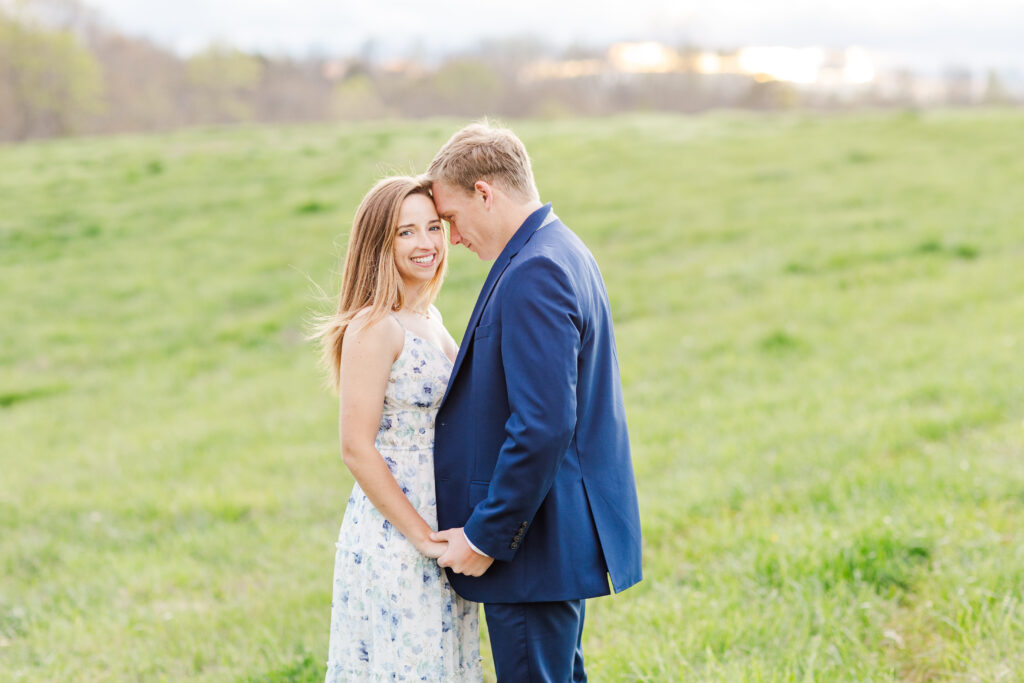 engaged couple wearing a blue, flowery dress and a navy blue suite smiling at Spring Grove Ranch