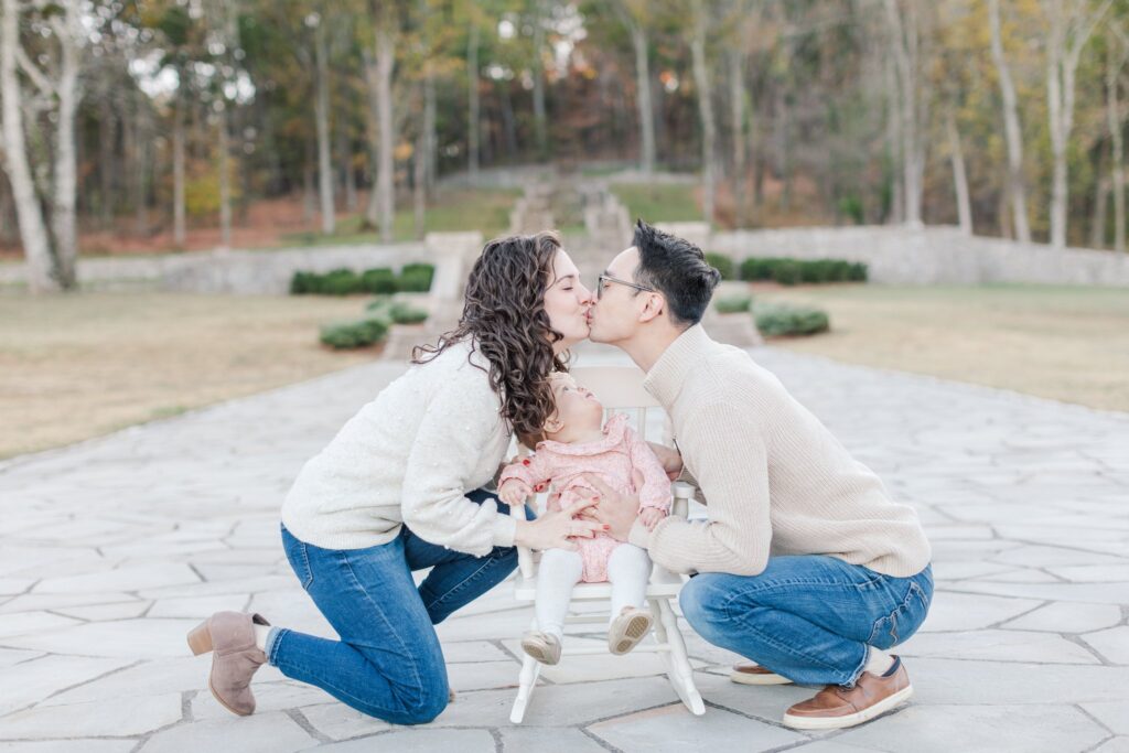 Husband and wife kissing at Percy Warner Park Steps while their 1 year old daughter stares up at them