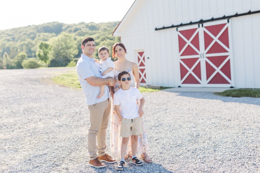 family standing together and smiling while standing by a white and red barn at Smith Park in Brentwood, TN which is one of the Best Nashville Family Session Locations!