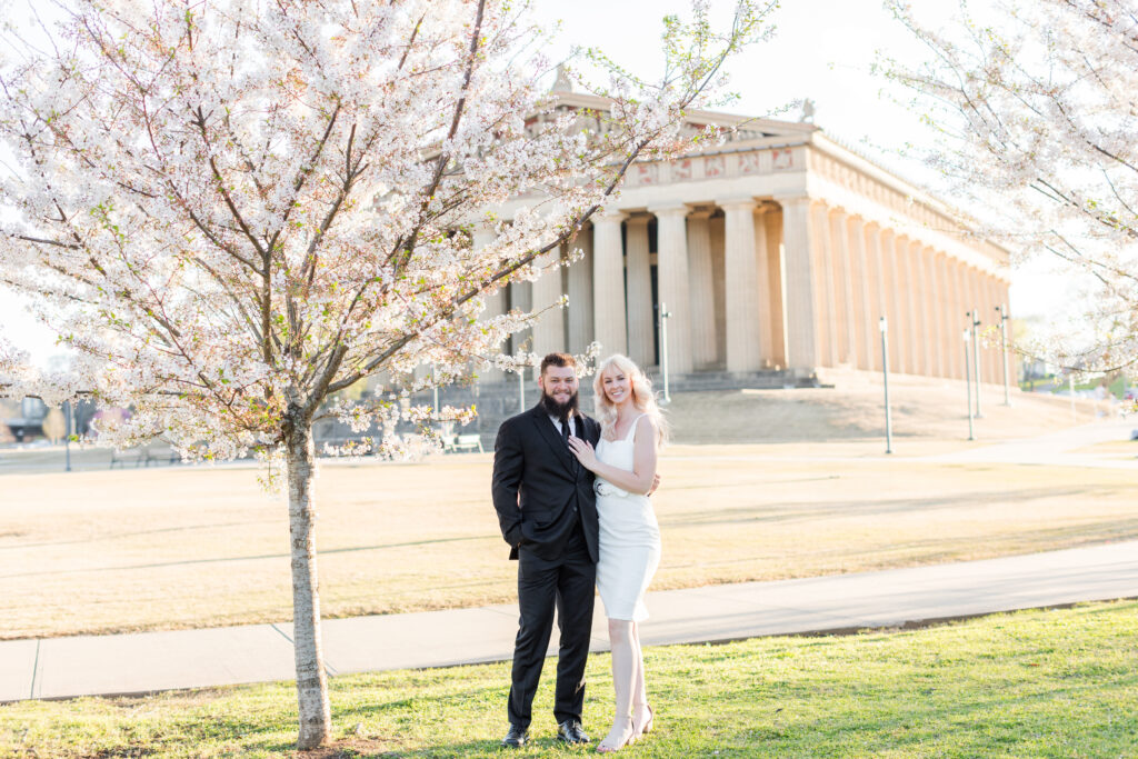 Couple wearing a white dress and black suite, smiling outside the Nashville Parthenon, which is one of the Best Nashville Family Session Locations! 