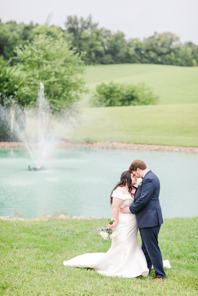 bride and groom posing for a photo by a pond at the White Dove Barn