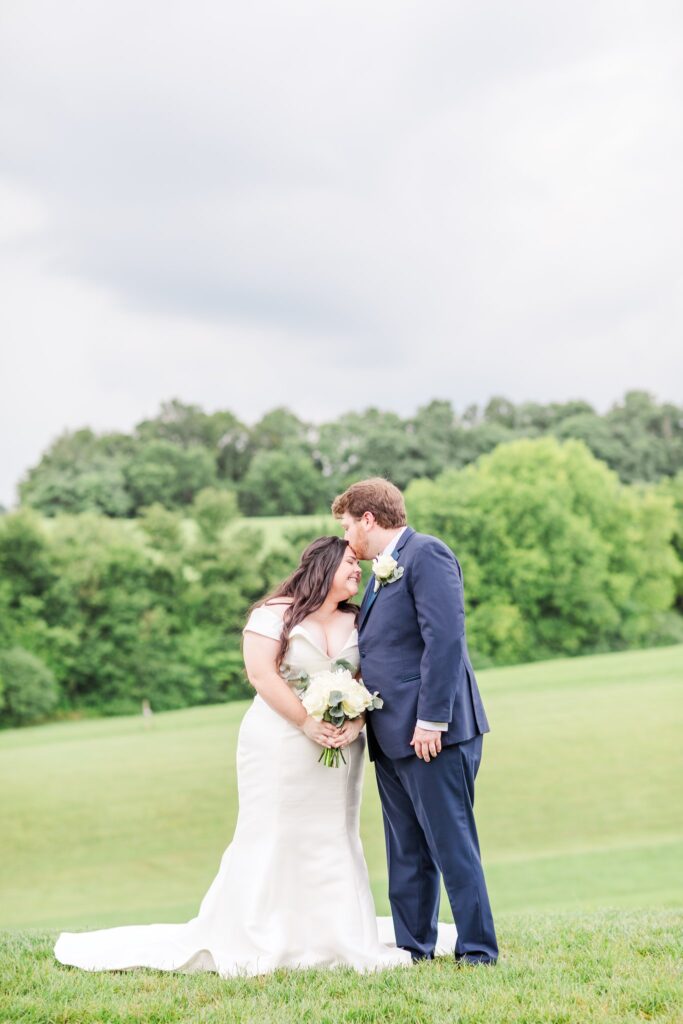 groom kissing bride's forehead in a field at The White Dove Barn