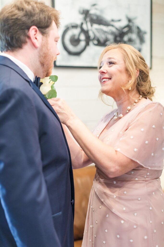 Mom helping groom put on his boutonniere in the Groom's Suite at the White Dove Barn