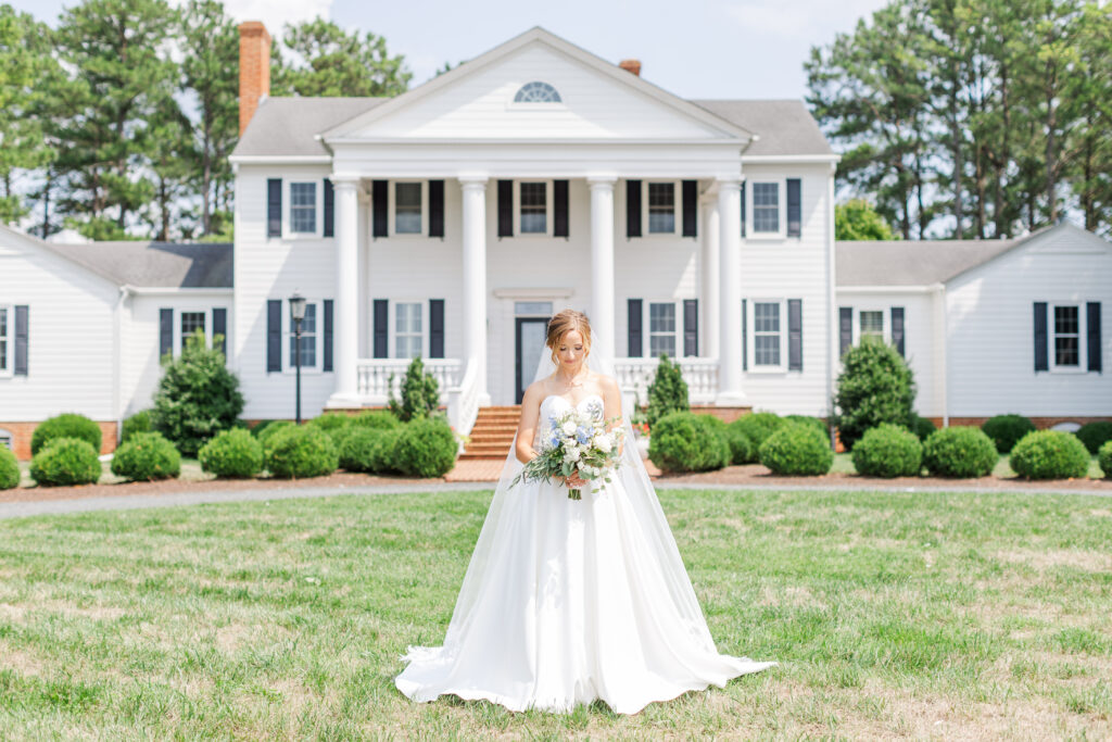 Bride looking down at her bouquet in front of Spring Grove Ranch Manor House on her wedding day