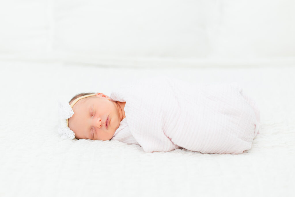 Baby laying on a white bed in her pink swaddle