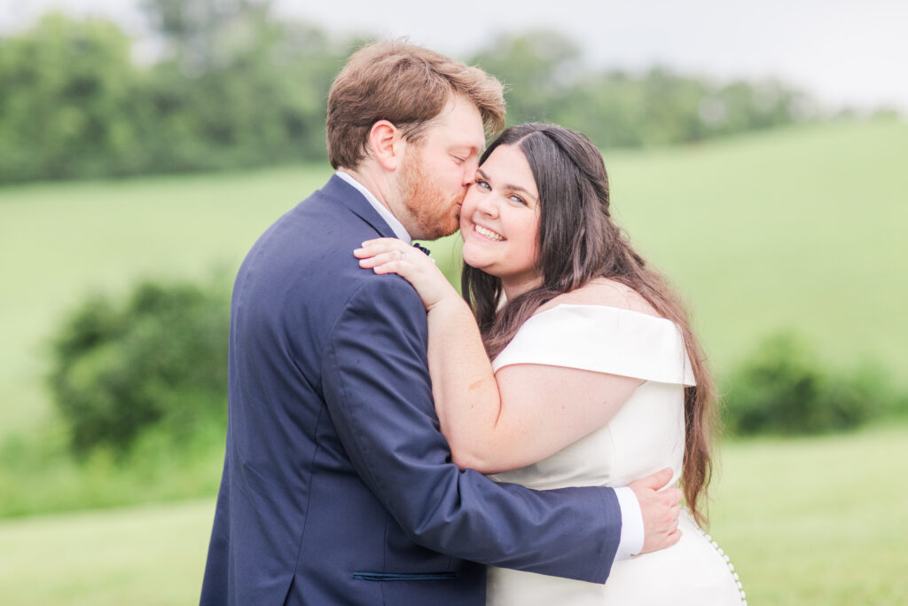 groom kissing his wife in a field at their White Dove Barn Wedding Day